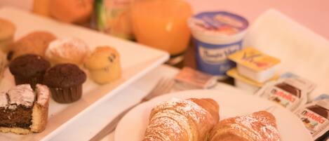 A breakfast table with pastries, a plate of muffins, a glass of orange juice, and a container of yogurt.