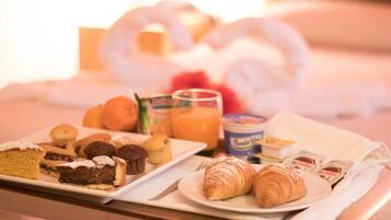 Ein Frühstücksbrett mit Gebäck, Muffins und Saft auf einem Hotelbett.