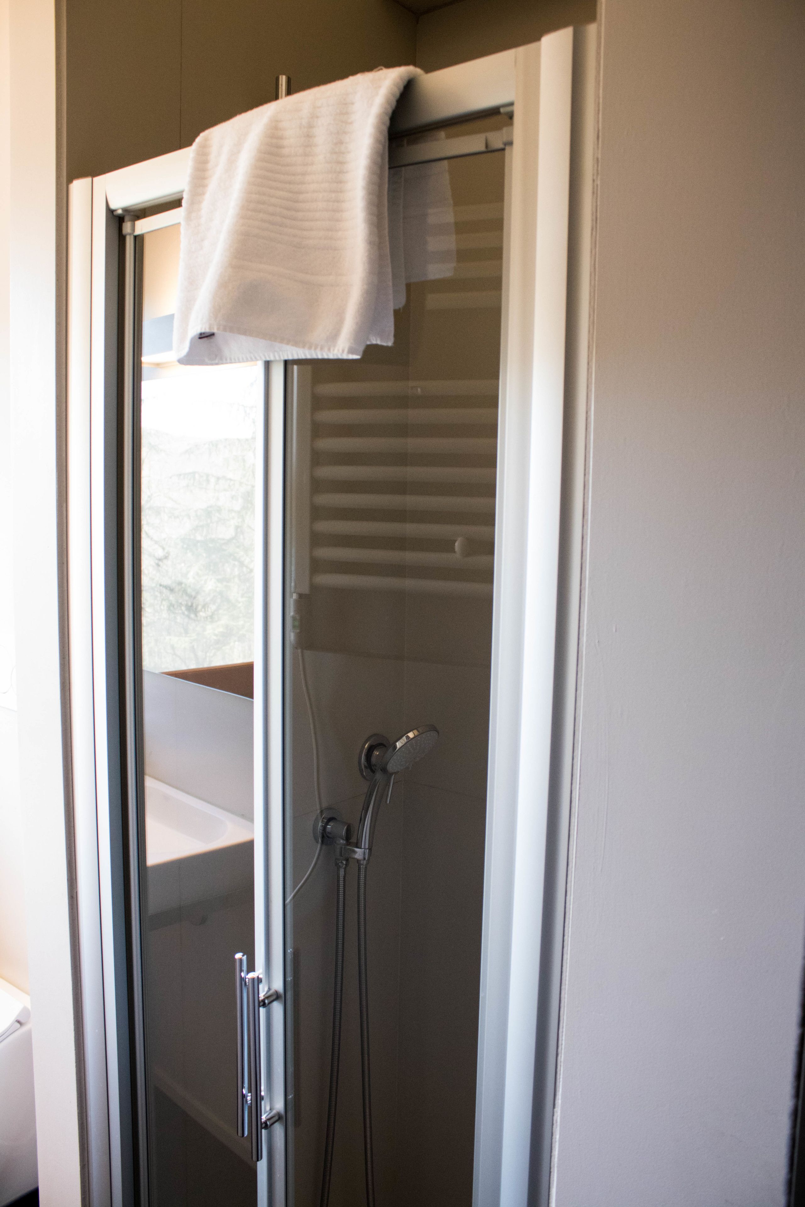 A bathroom with a glass shower enclosure, a towel hanging on the door, and a visible window.