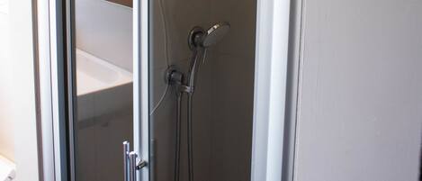 A bathroom with a glass shower enclosure, a towel hanging on the door, and a visible window.