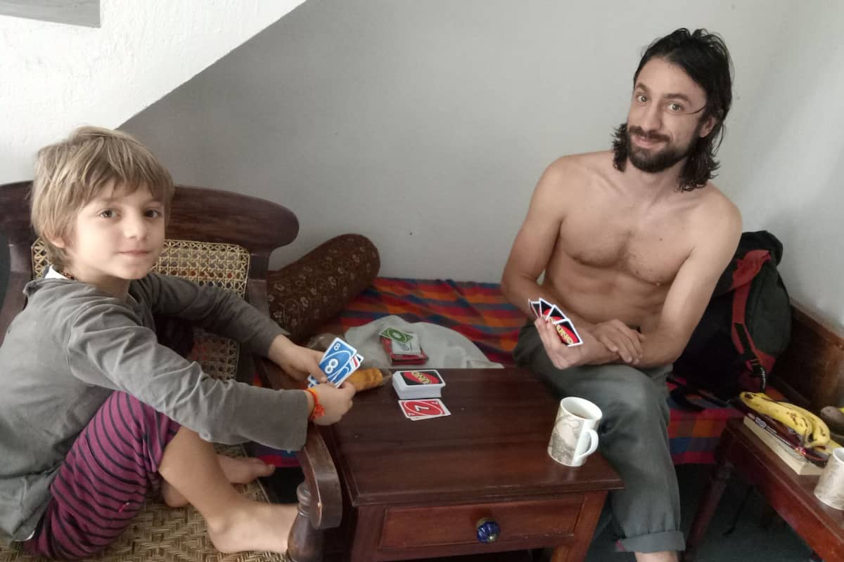 Two people sitting on a bed with a wooden nightstand between them.