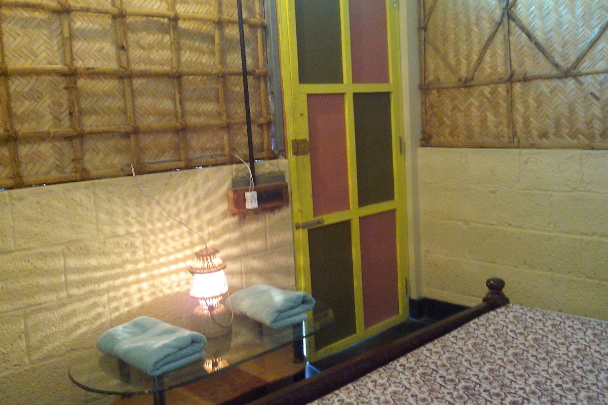 A room with a bed, a table with towels, a lamp, and a door with a window.