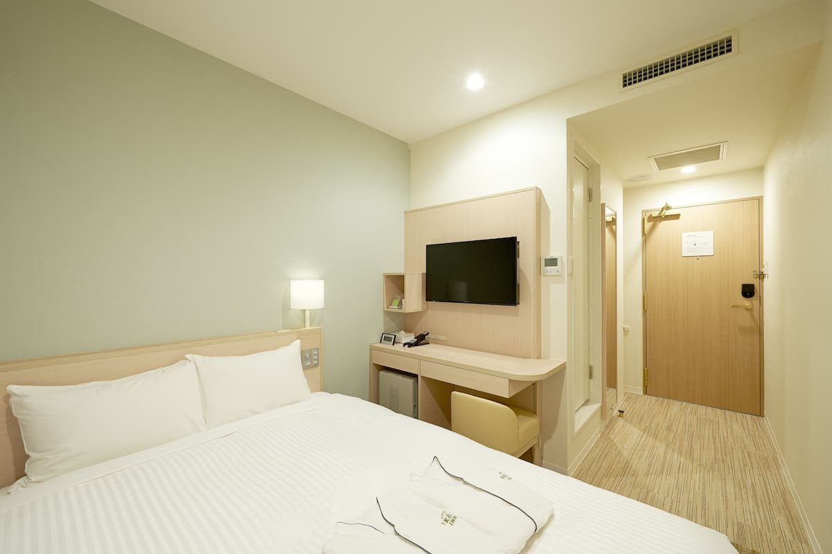 A hotel room with a bed, a desk, a TV, and a door.