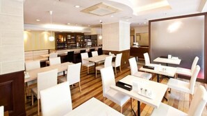 A modern restaurant with white tables and chairs, a bar area, and a large mirror.