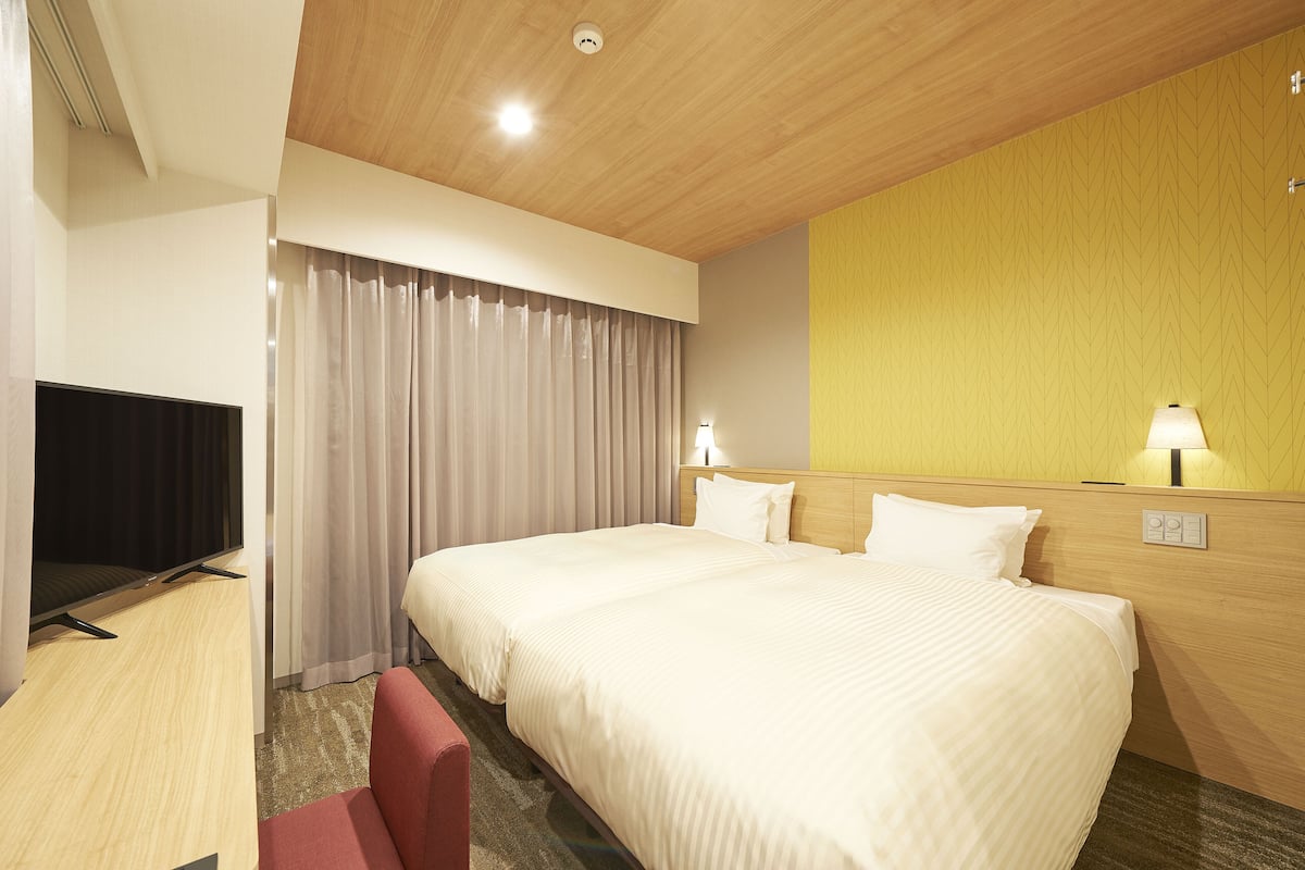 A hotel room with a large bed, a flat-screen TV, a desk, and a red chair.