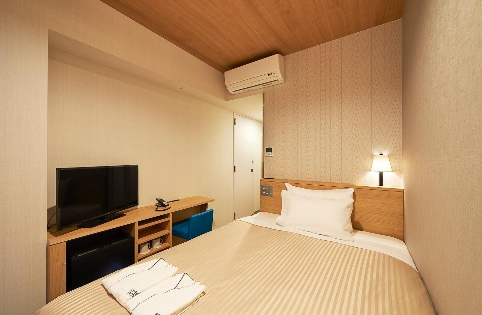 Hotellihuone, jossa on sänky, televisio, työpöytä, lamppu ja ilmastointilaite.