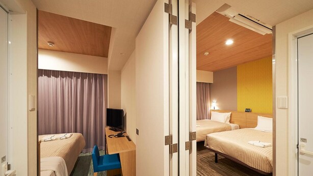 A hotel room with two beds, a desk with a chair, a television, and a bathroom door.
