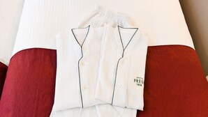 A neatly folded white pajama set with a label on the side, placed on a bed with a red pillow.
