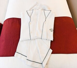 A neatly folded white pajama set with a label on the side, placed on a bed with a red pillow. - Sotetsu Fresa Inn Tokyo Tamachi (Tokyo)