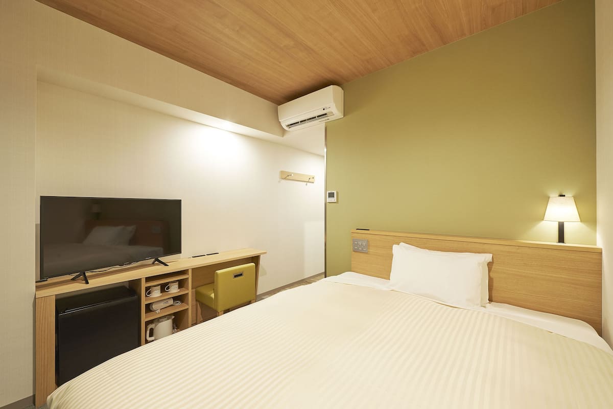 A hotel room with a bed, a TV, a desk, and a lamp.