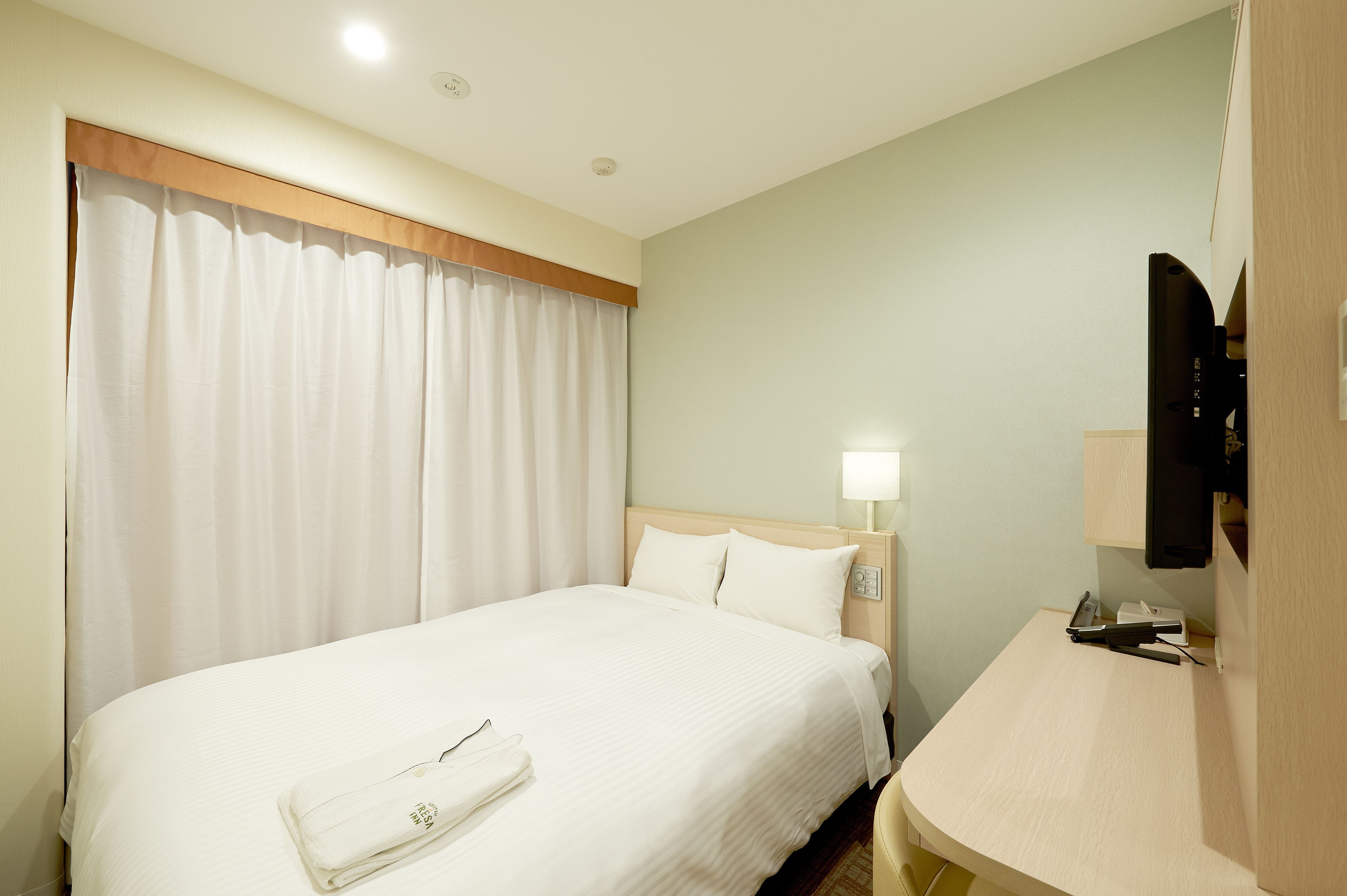 Une chambre d’hôtel avec un lit, une table de chevet, une lampe et un téléviseur.