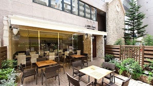 An outdoor dining area with tables and chairs, a stone wall, and a wooden fence. - Sotetsu Fresa Inn Tokyo Tamachi (Tokyo)