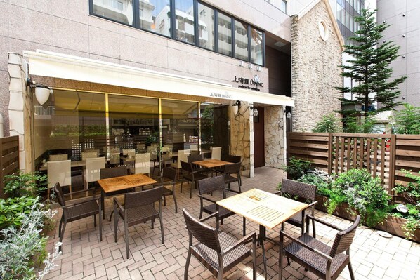 An outdoor dining area with tables and chairs, a stone wall, and a wooden fence. - Sotetsu Fresa Inn Tokyo Tamachi (Tokyo)