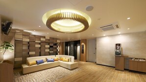 A modern lobby with a sectional sofa, a wooden floor, a unique circular ceiling light, and a small coffee station. - Sotetsu Fresa Inn Tokyo Tamachi (Tokyo)