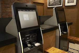 A self-service kiosk with a touchscreen interface, a receipt printer, and a card reader.