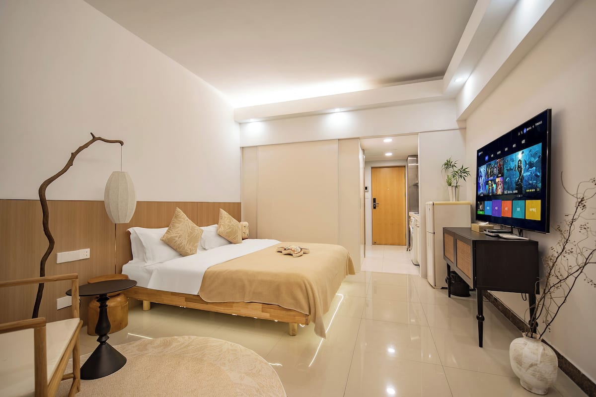 Una habitación de hotel moderna con cama, mesita de noche, lámpara, televisión y una planta pequeña.
