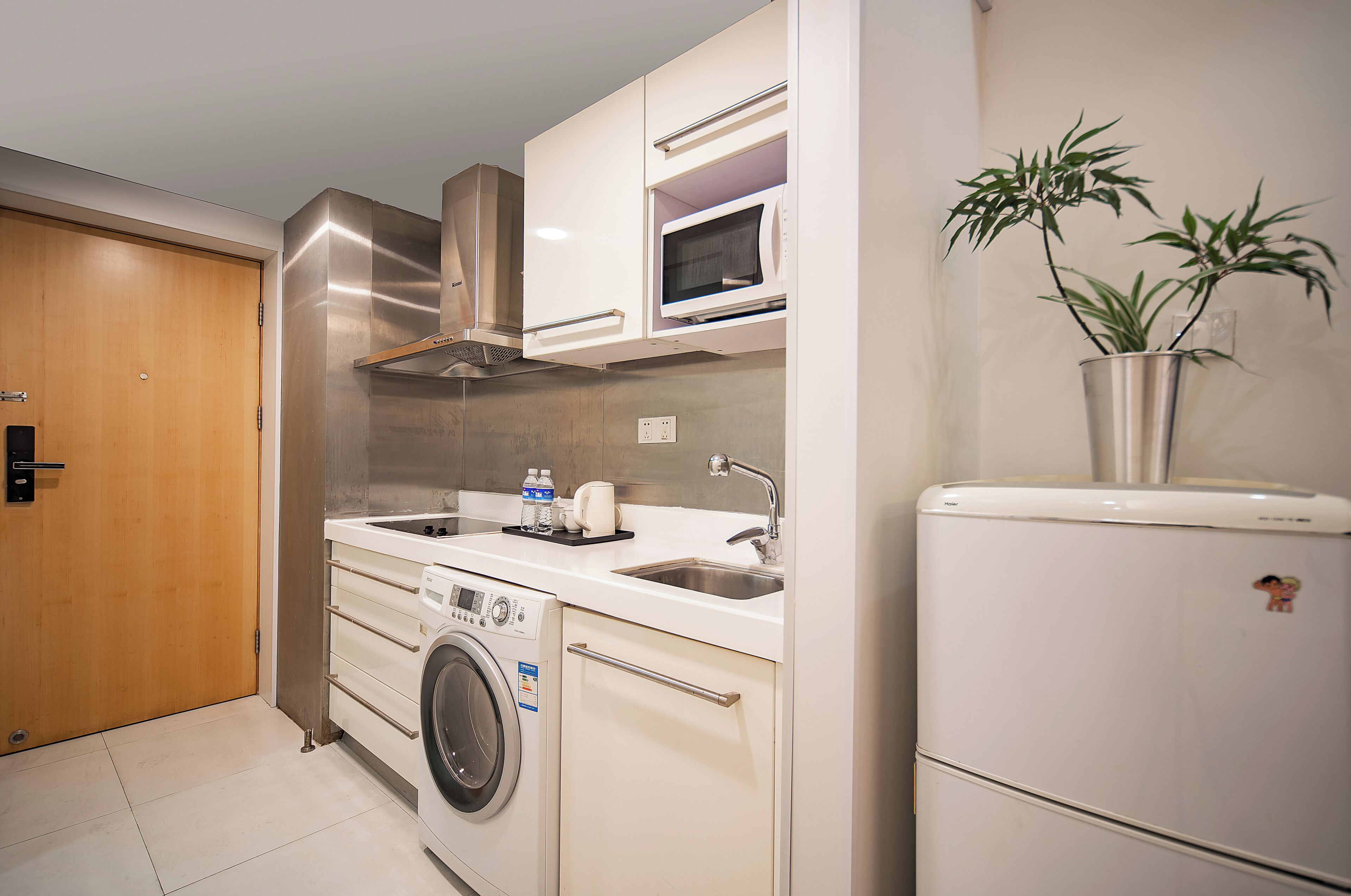 A compact kitchen with a washing machine, microwave, and a refrigerator.