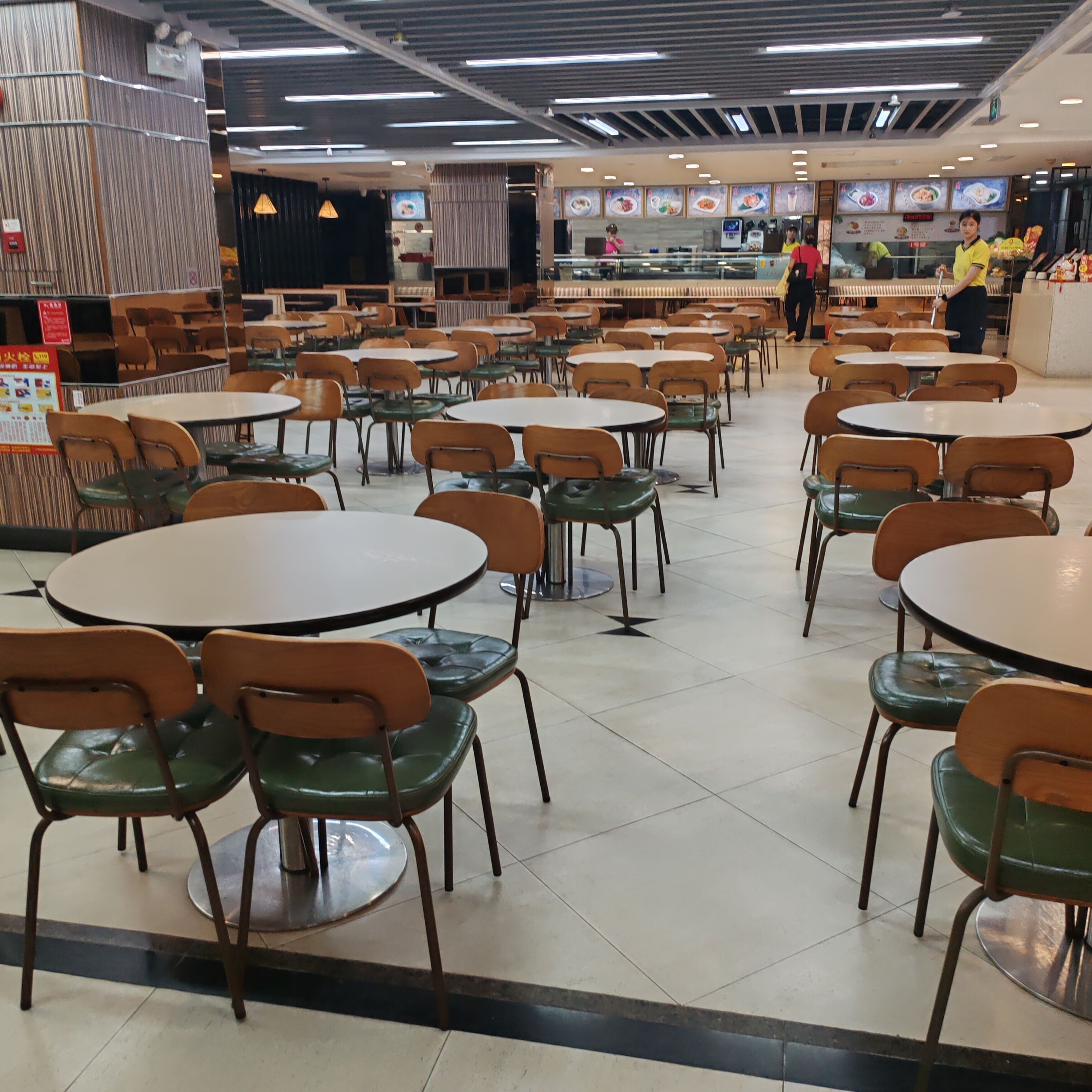 Una cafetería con mesas y sillas redondas, una barra de comida y un suelo de baldosas.