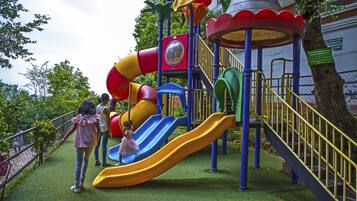 Children can play safely in this fenced playground featuring slides and climbing elements.