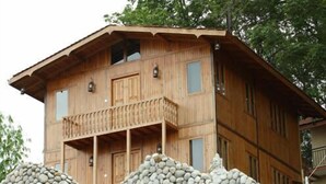 Eine zweistöckige Holzhütte mit einem Balkon im zweiten Stock, umgeben von einer Steinmauer.