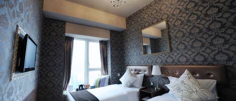 Ein Hotelzimmer mit zwei Betten, einer Kandelaber, einem großen Spiegel und Wandtapete mit Muster.
