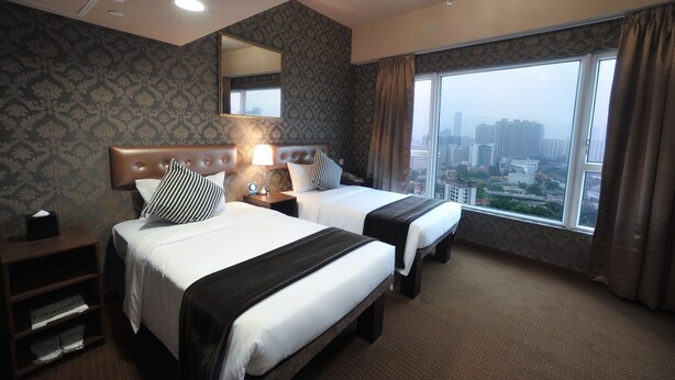 A hotel room with two beds, a large window with a city view, a chandelier, and a mirror on the wall. - Ramada Grand Tsim Sha Tsui (Former Ramada Hong Kong Grand Tsim Sha Tsui) (Kowloon)