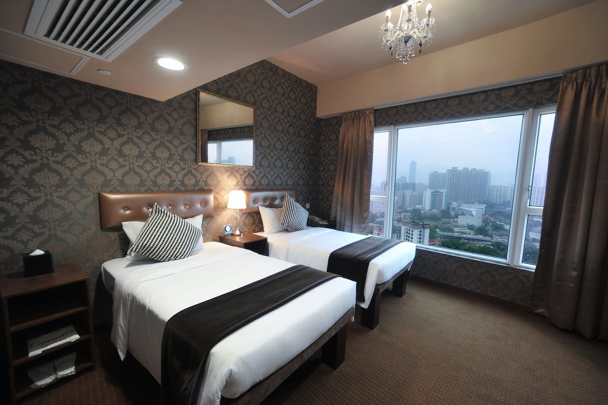 A hotel room with two beds, a large window with a city view, a chandelier, and a mirror on the wall.
