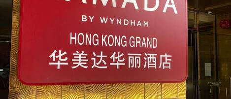 Schild für das Ramada by Wyndham Hong Kong Grand Hotel mit einer goldverzierten Wand im Hintergrund.