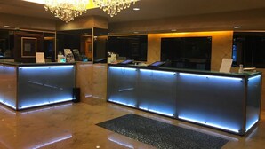 A reception area with a modern design, featuring a large chandelier and a glass reception desk with illuminated edges. - Ramada Grand Tsim Sha Tsui (Former Ramada Hong Kong Grand Tsim Sha Tsui) (Kowloon)