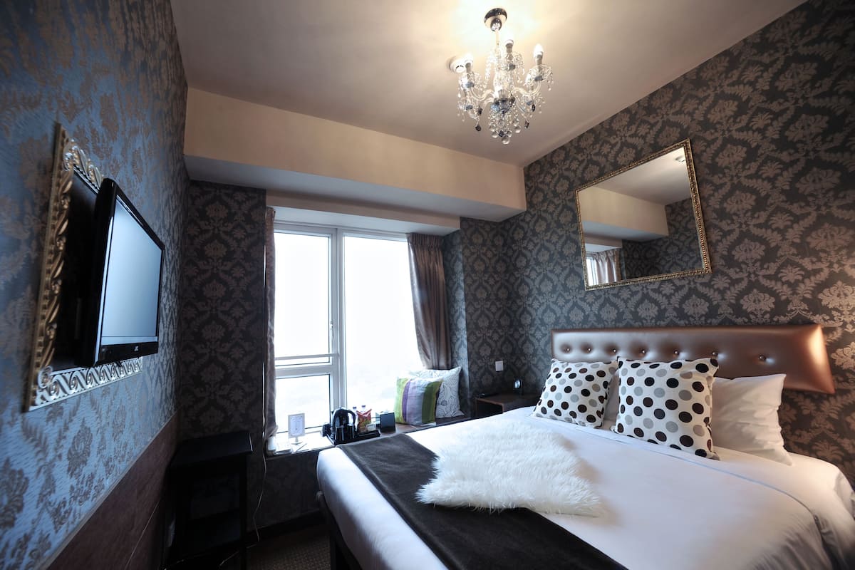 A hotel room with a large bed, a television, a chandelier, and patterned wallpaper.