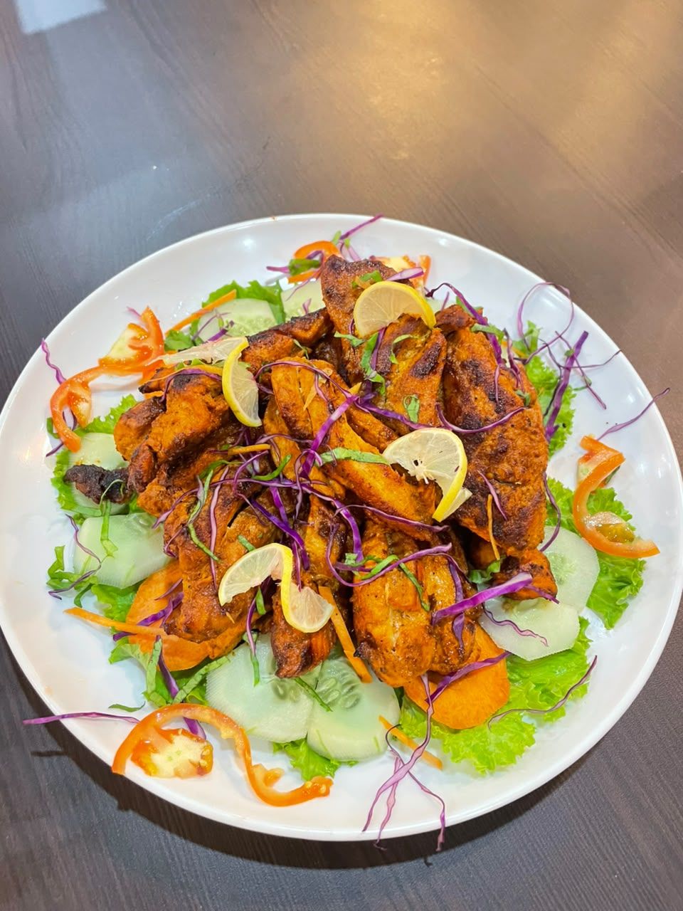 A plate of grilled chicken with vegetables and a lemon wedge.
