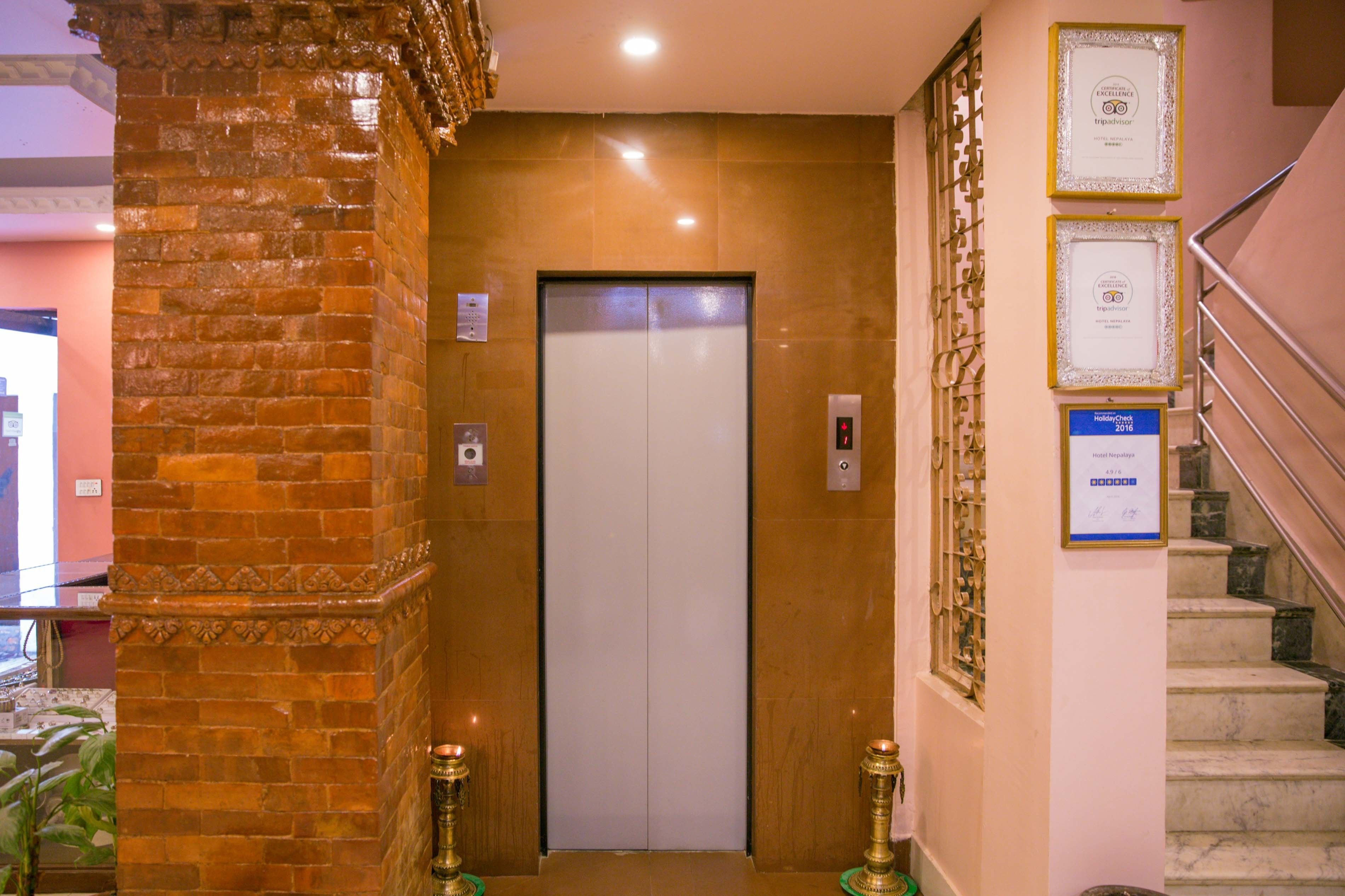 An elevator with a modern design, flanked by a brick pillar and a staircase with a metal railing.