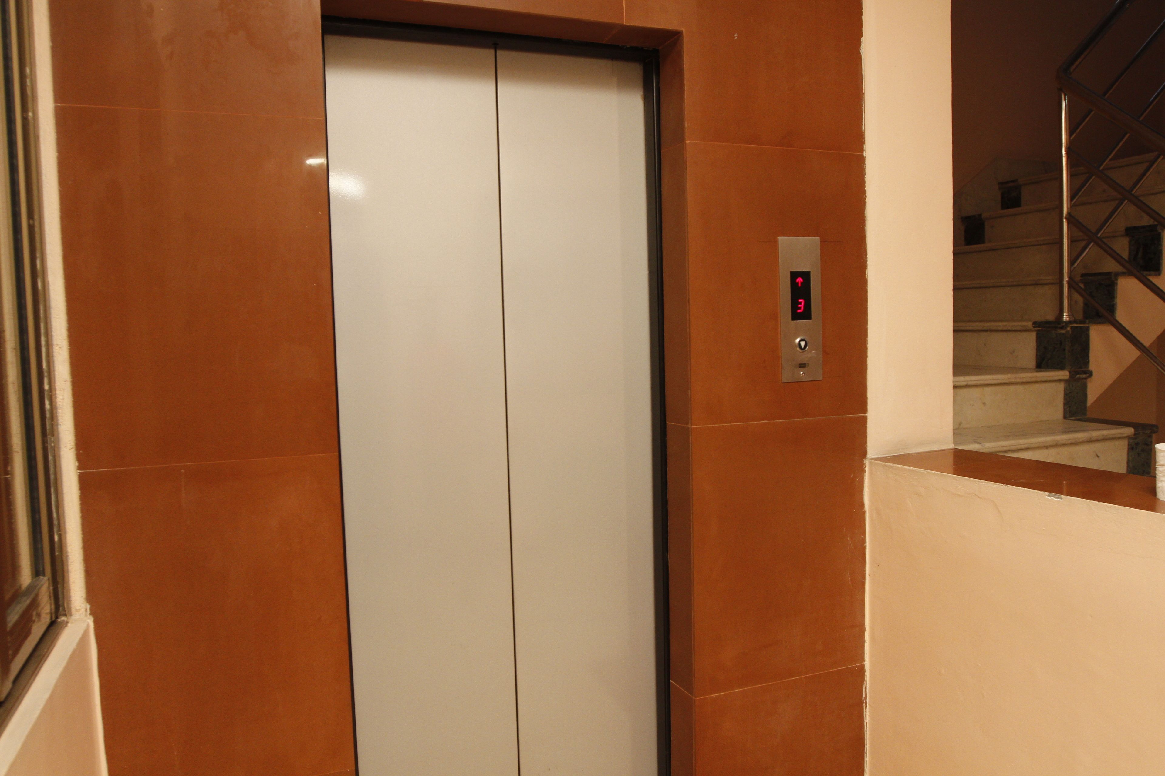 An elevator with a control panel, a staircase, and a wall with a reflective surface.