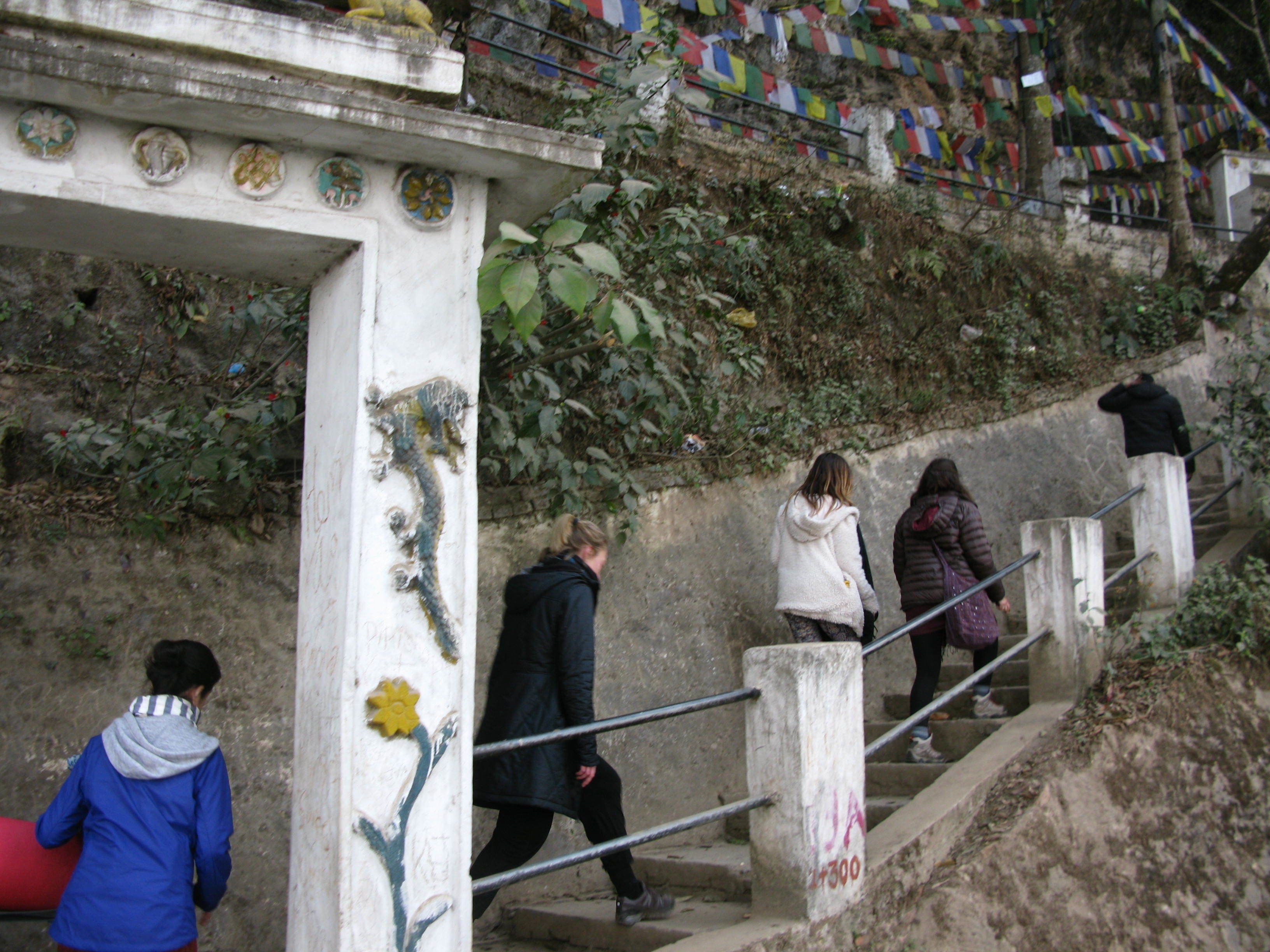Eine Treppe mit Geländer, eine Person geht hinunter, und bunte Gebetsfahnen an einer Wand.