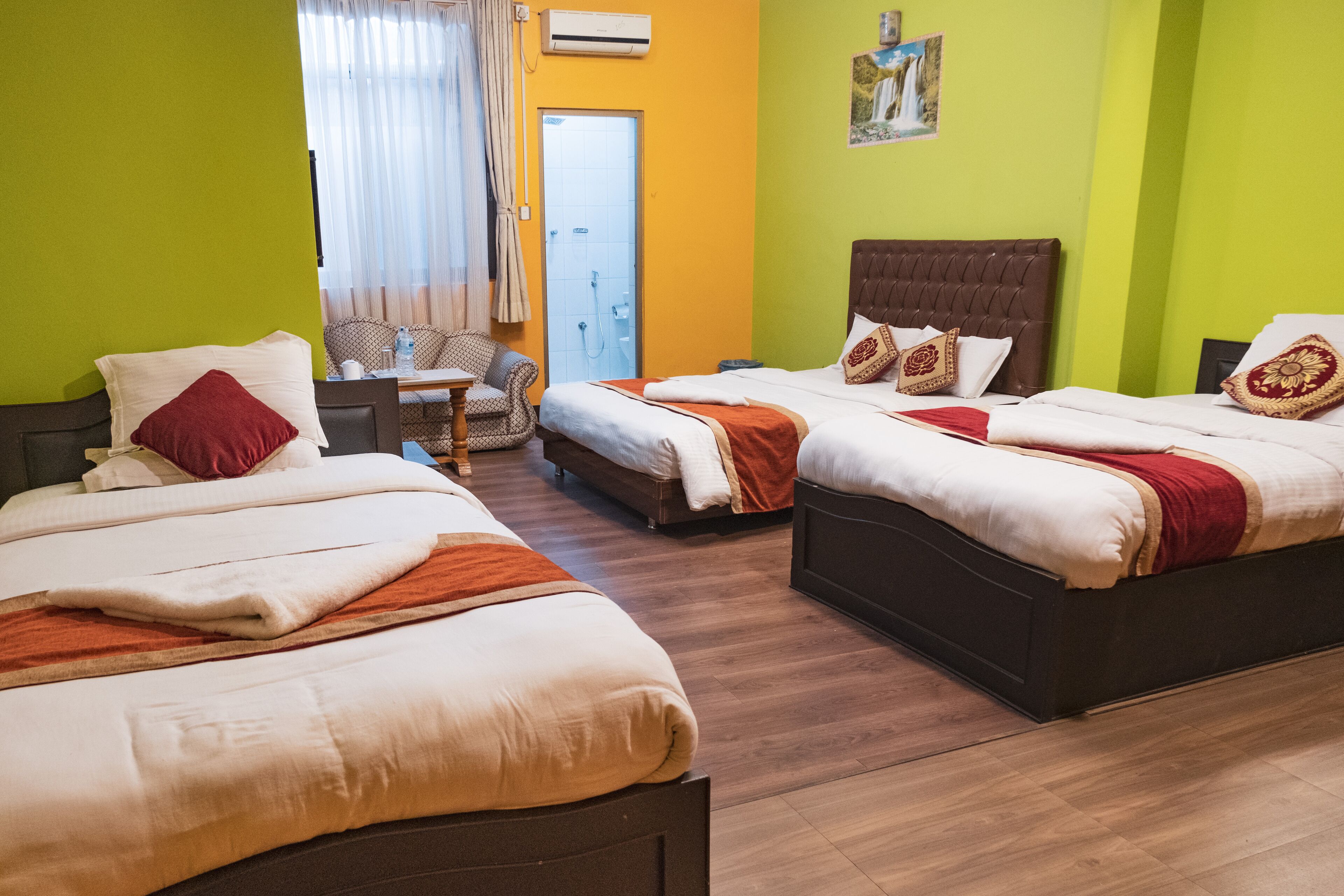 A hotel room with two beds, a chair, a small table, and a door leading to a bathroom.