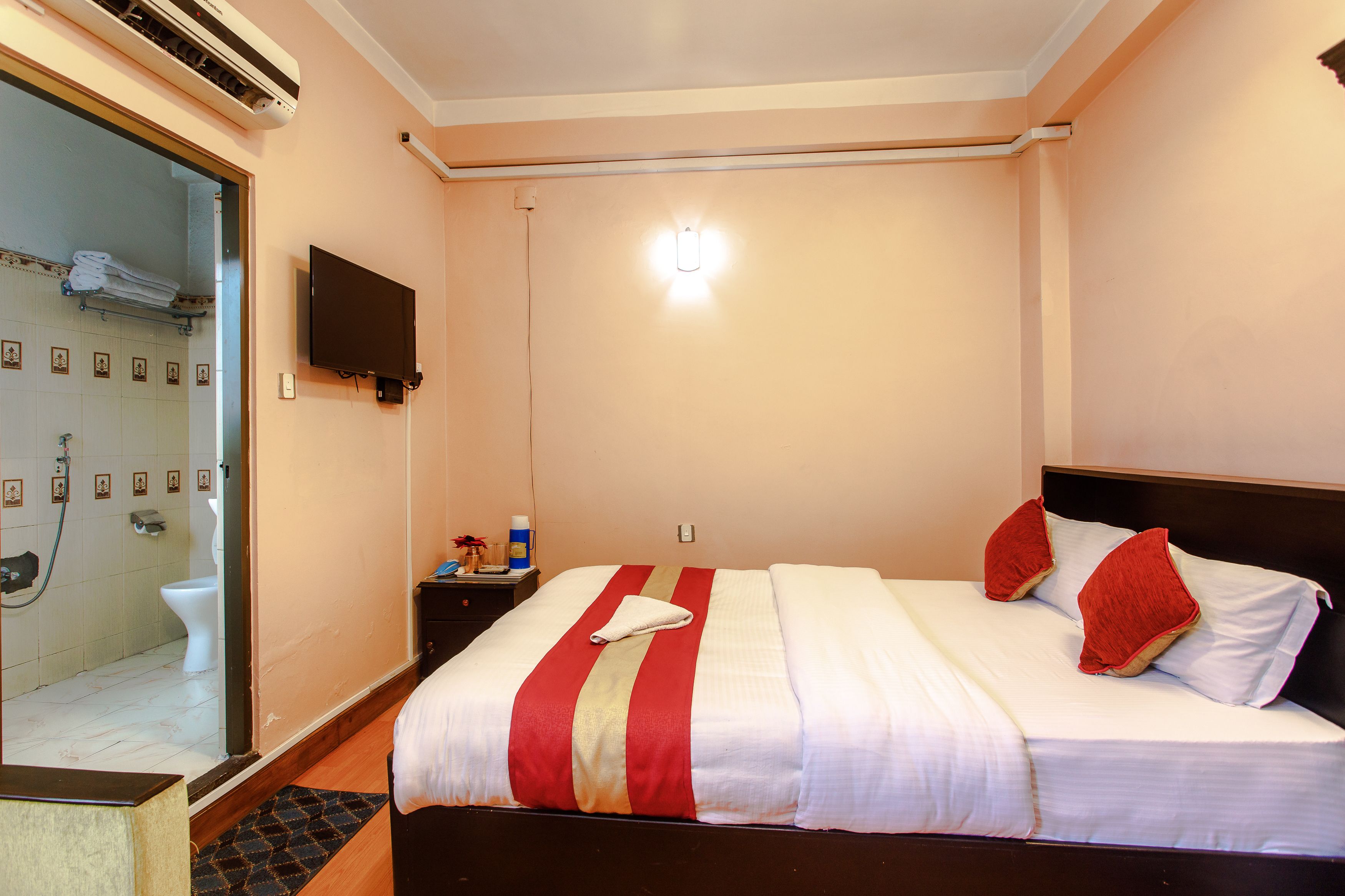 A hotel room with a bed, a TV, a bathroom with a shower, and a towel rack.