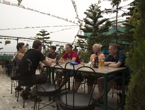 A group of people seated around a table with chairs, under a tent-like structure with string lights, surrounded by greenery. - Hotel Nepalaya (Kathmandu)