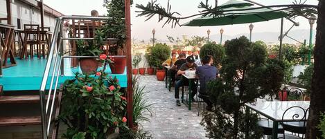 An outdoor café with tables and chairs, surrounded by potted plants and a staircase.