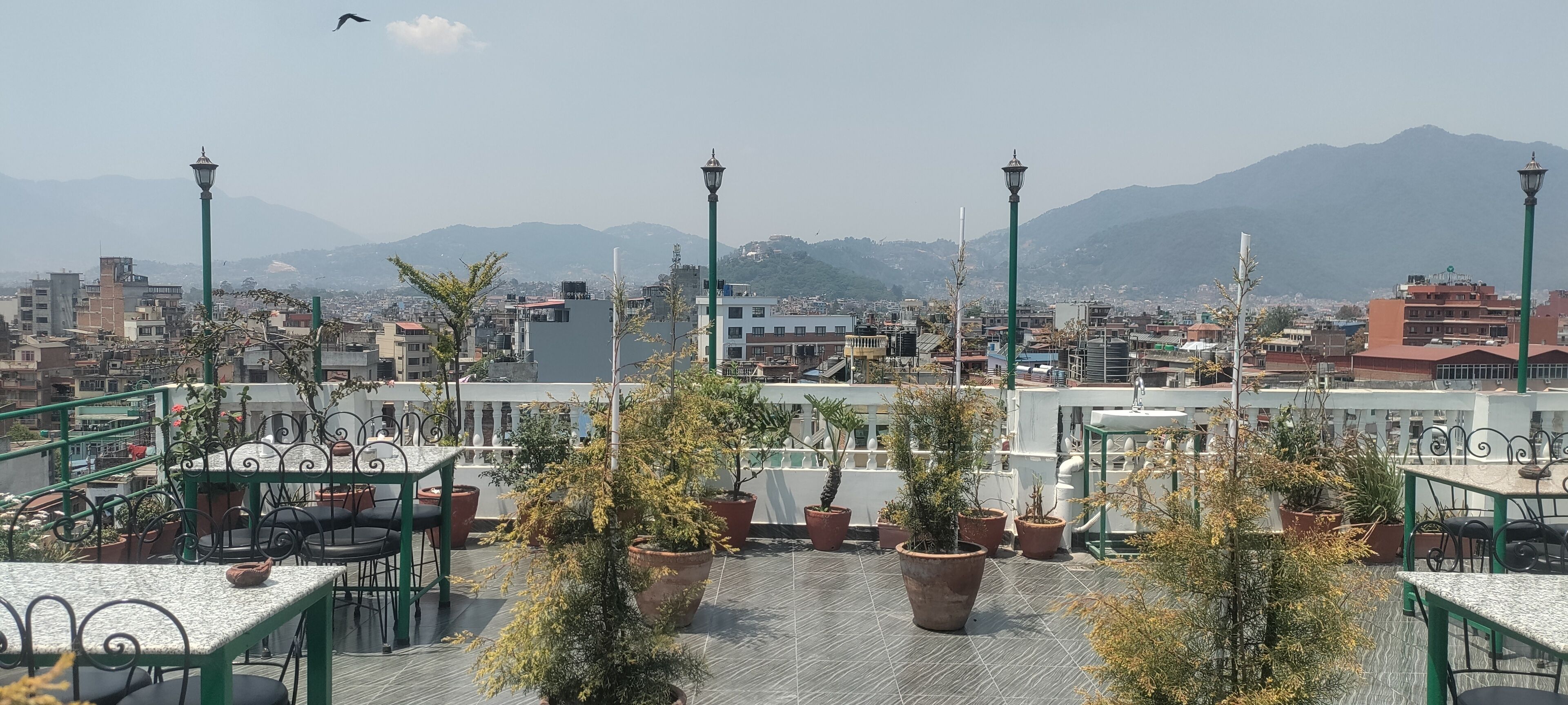 Une terrasse sur le toit agrémentée de plantes en pot, de sièges d’extérieur et offrant une vue sur le paysage urbain, avec des montagnes en arrière-plan.