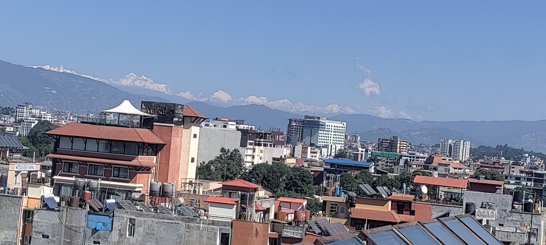 A cityscape with buildings, a tent-like structure, and snow-capped mountains in the background.