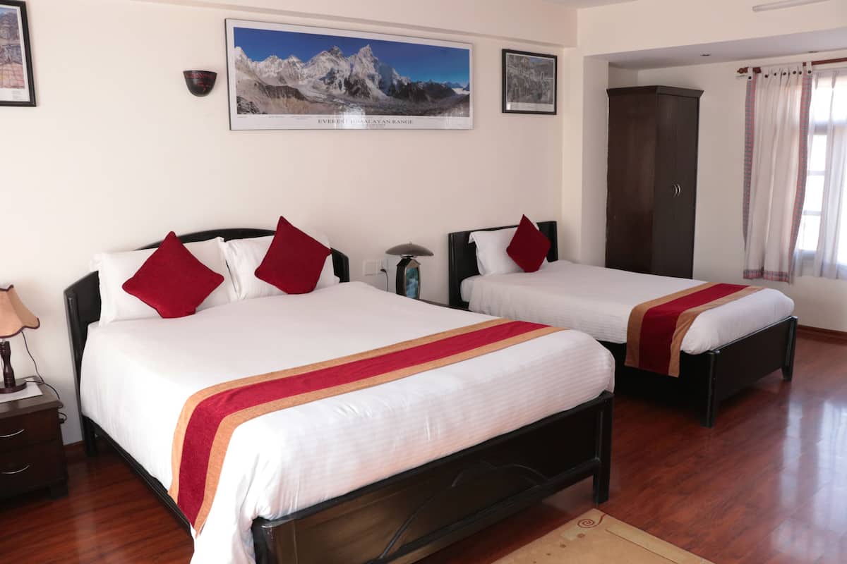 A hotel room with two beds, a wardrobe, a nightstand, and a framed picture of a mountain range on the wall.