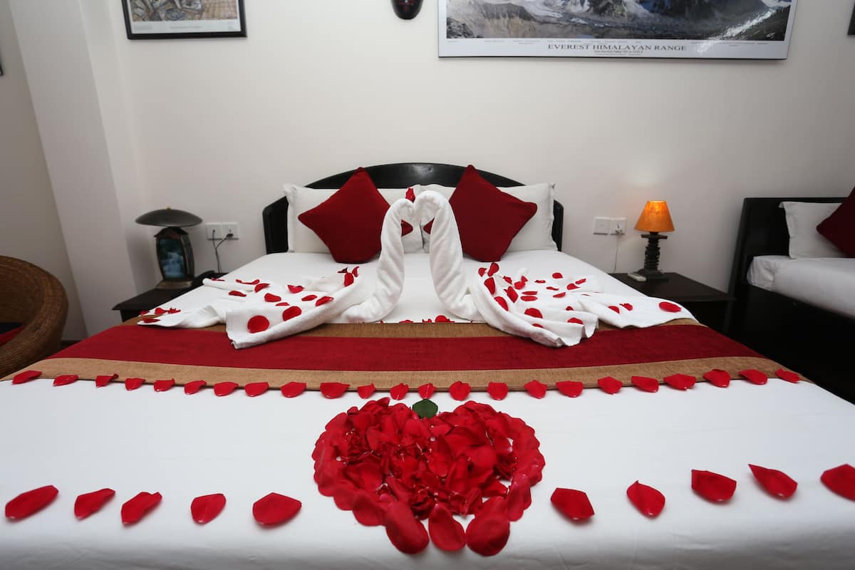 A neatly made bed with a heart-shaped arrangement of rose petals and a towel sculpture in the center.