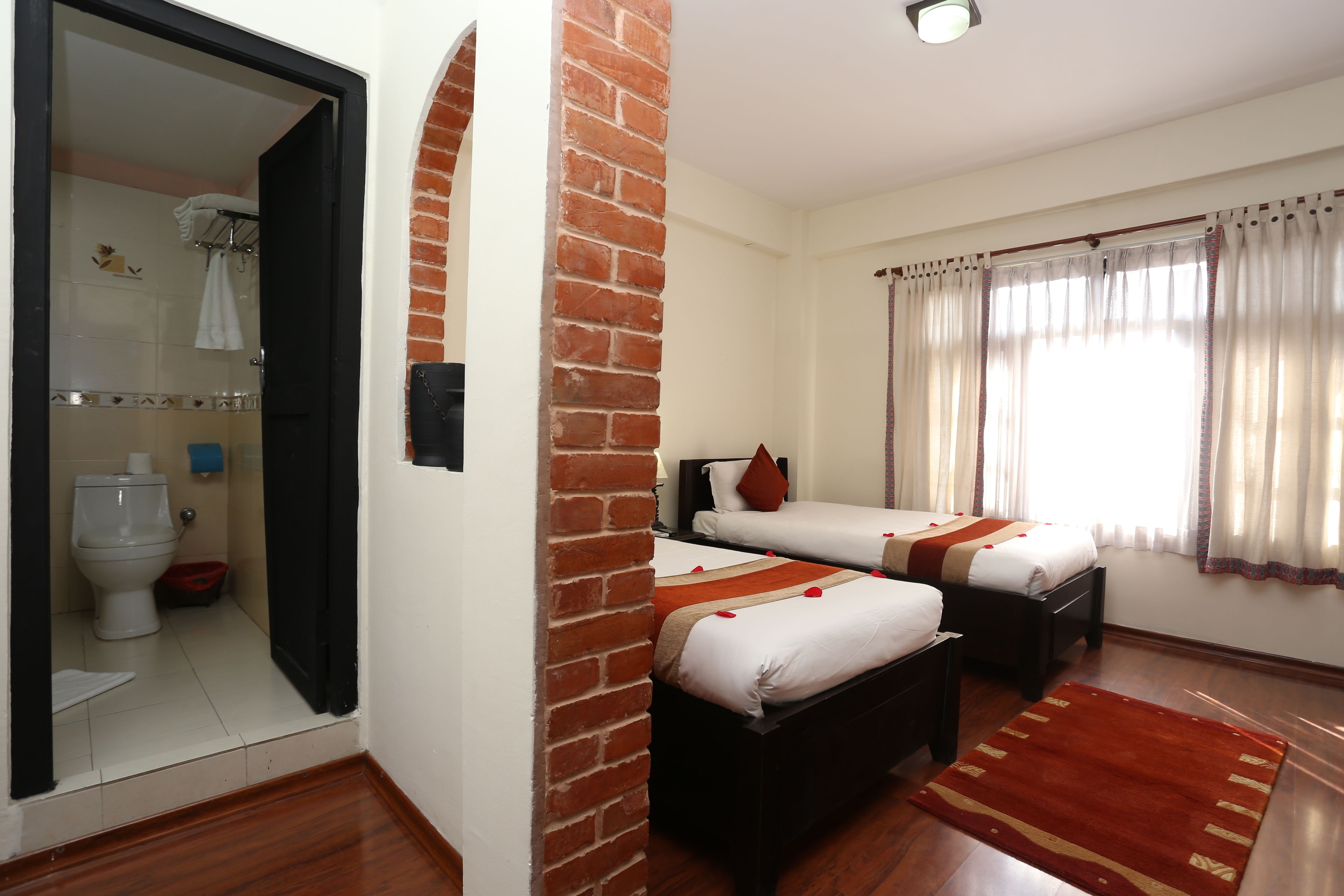A hotel room with two beds, a bathroom, and a wooden floor.