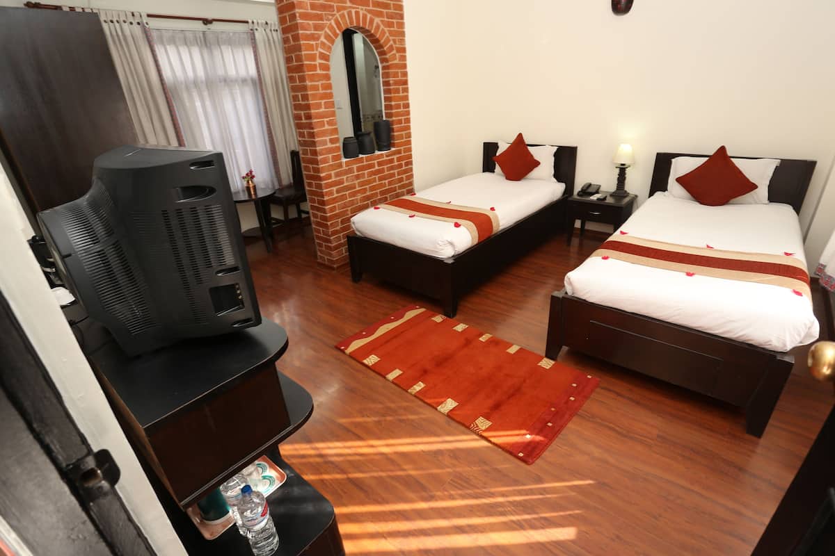 A hotel room with a TV, two beds, a brick wall, and a wooden floor.