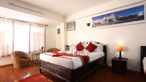 A neatly arranged bedroom with a large bed, a bedside table with a lamp, a chair, and a window with curtains. - Thamel Eco Resort (Kathmandu)