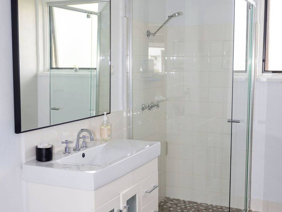 Un baño con tocador blanco, un espejo grande, cabina de ducha de cristal y baldosas de suelo estampadas.