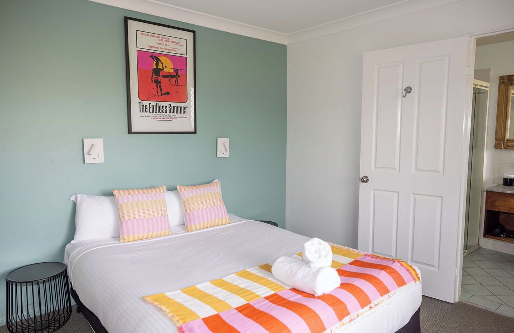 Une chambre d’hôtel avec un lit, des oreillers, une affiche au mur et une porte.