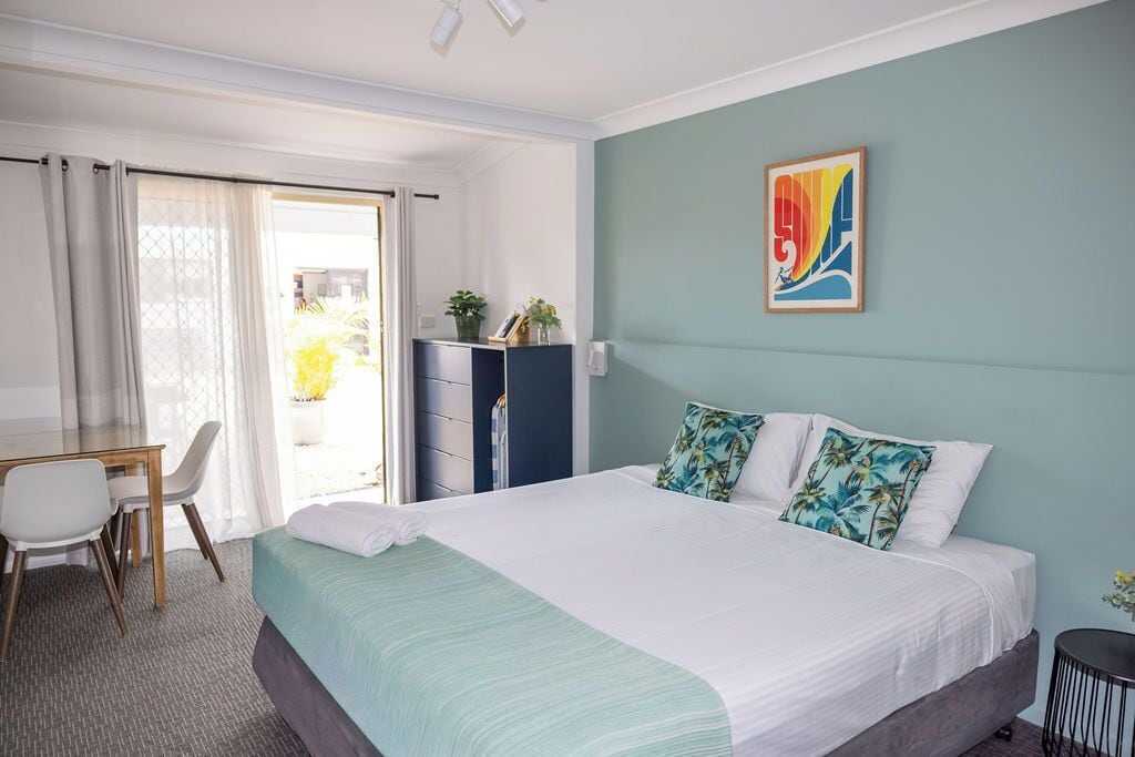 Een hotelkamer met een bed, een bureau, een stoel, een kast en een schilderij aan de muur.