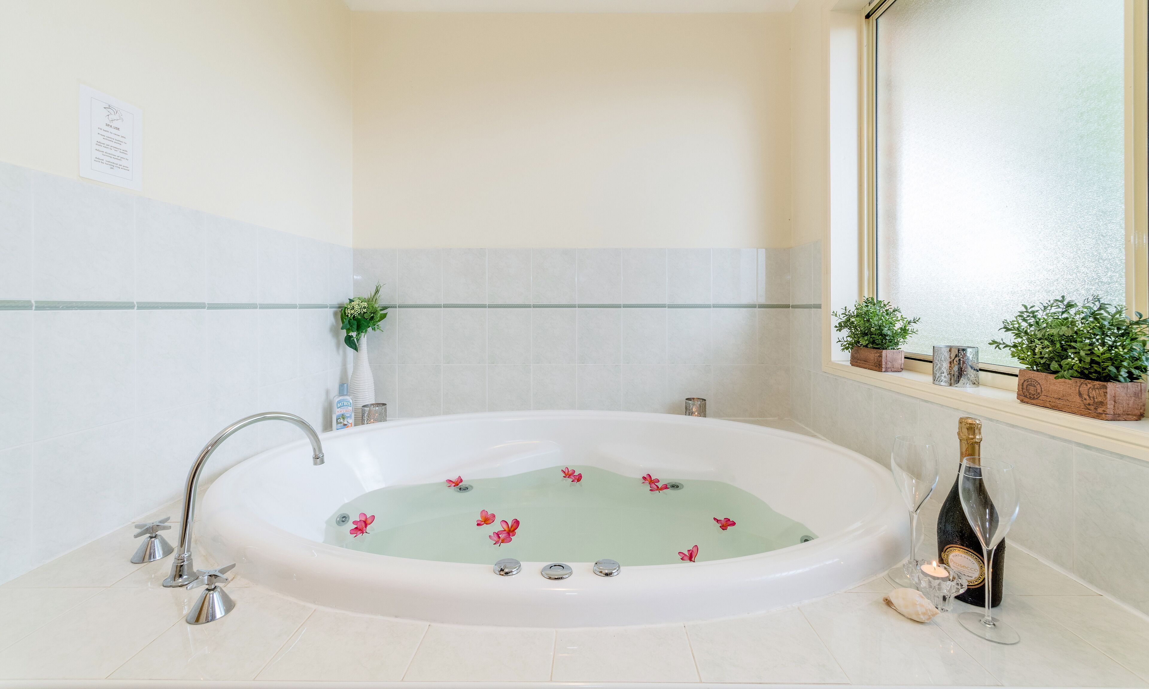 Un baño con una bañera independiente, una ventana con plantas y una botella de champán.