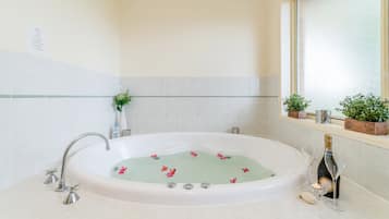 Un baño con una bañera independiente, una ventana con plantas y una botella de champán.